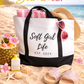 Beach scene with a tote bag labeled 'Soft Girl Life EST. 2024', sunglasses, and beach accessories on sand with 'Hello Summer' text and beach elements.